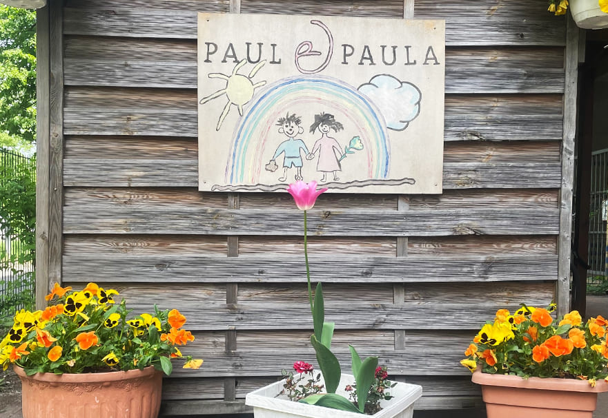 Holztafel mit dem Logo der Kita Paul und Paula, dekoriert mit bunten Blumen